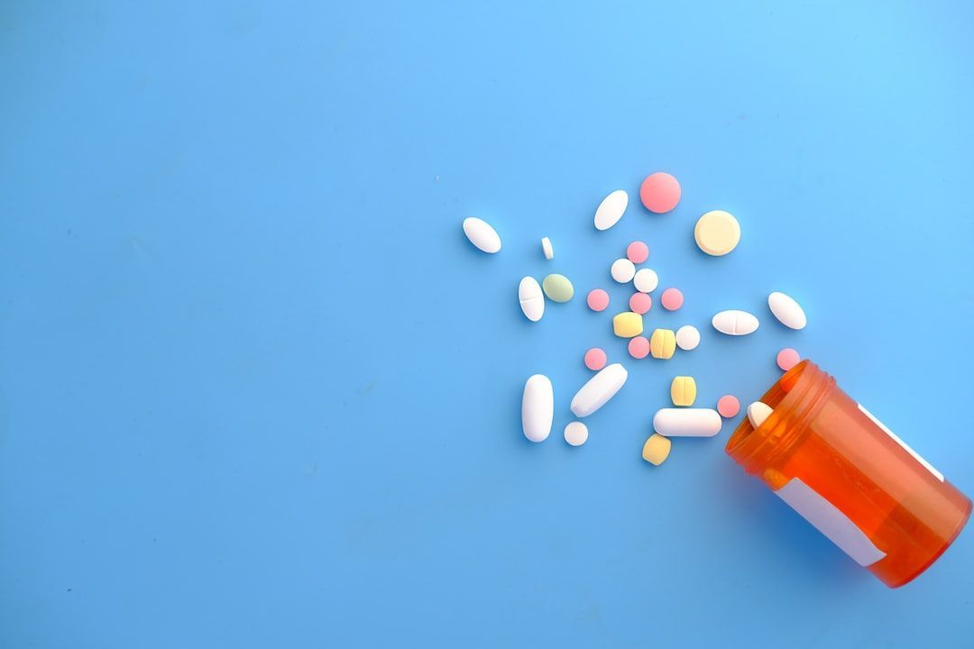 Orange pill bottle tipped over, spilling various colorful pills on a blue surface.