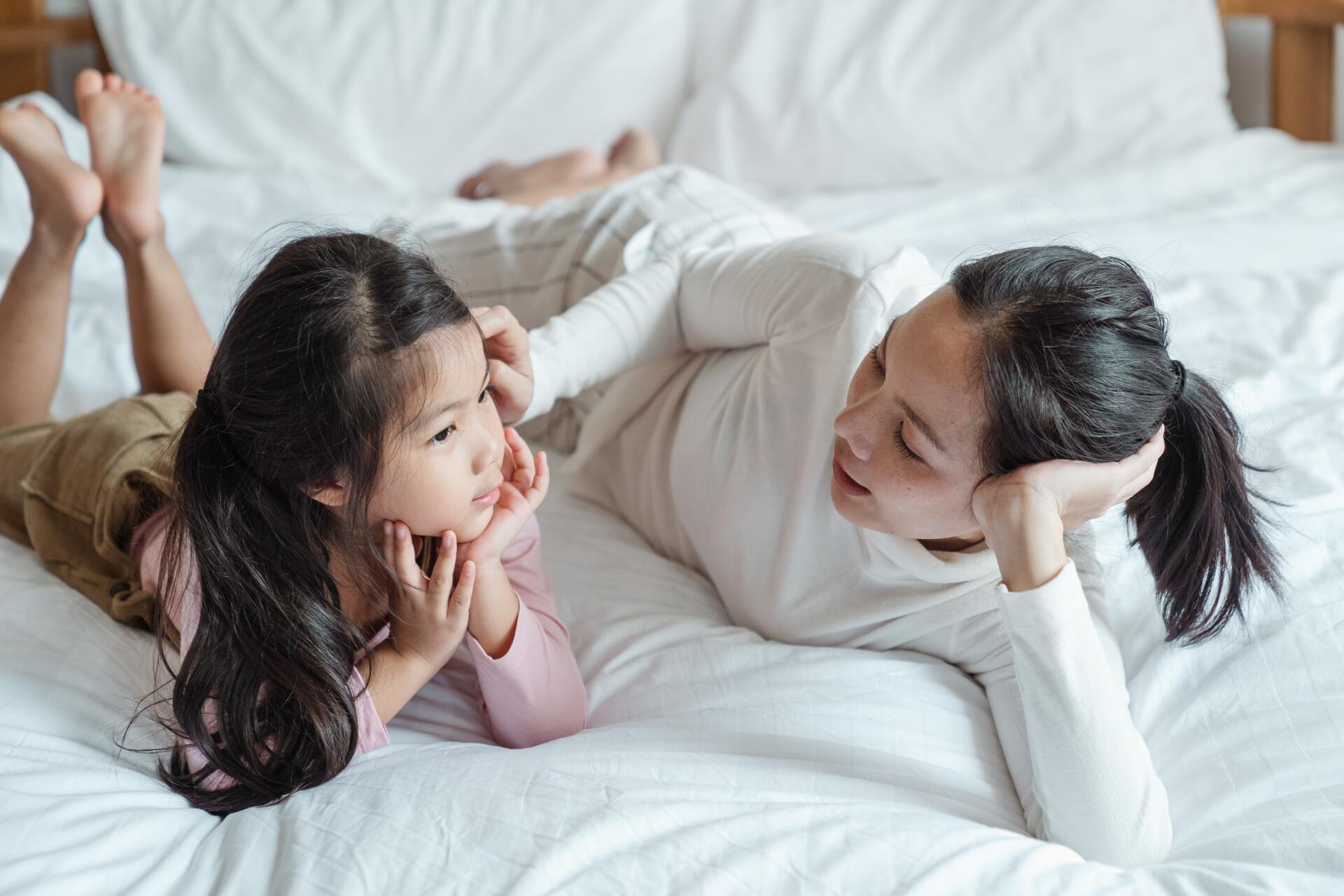 Mother and child lying on a bed, talking. Both are looking at each other, and the child is listening intently.
