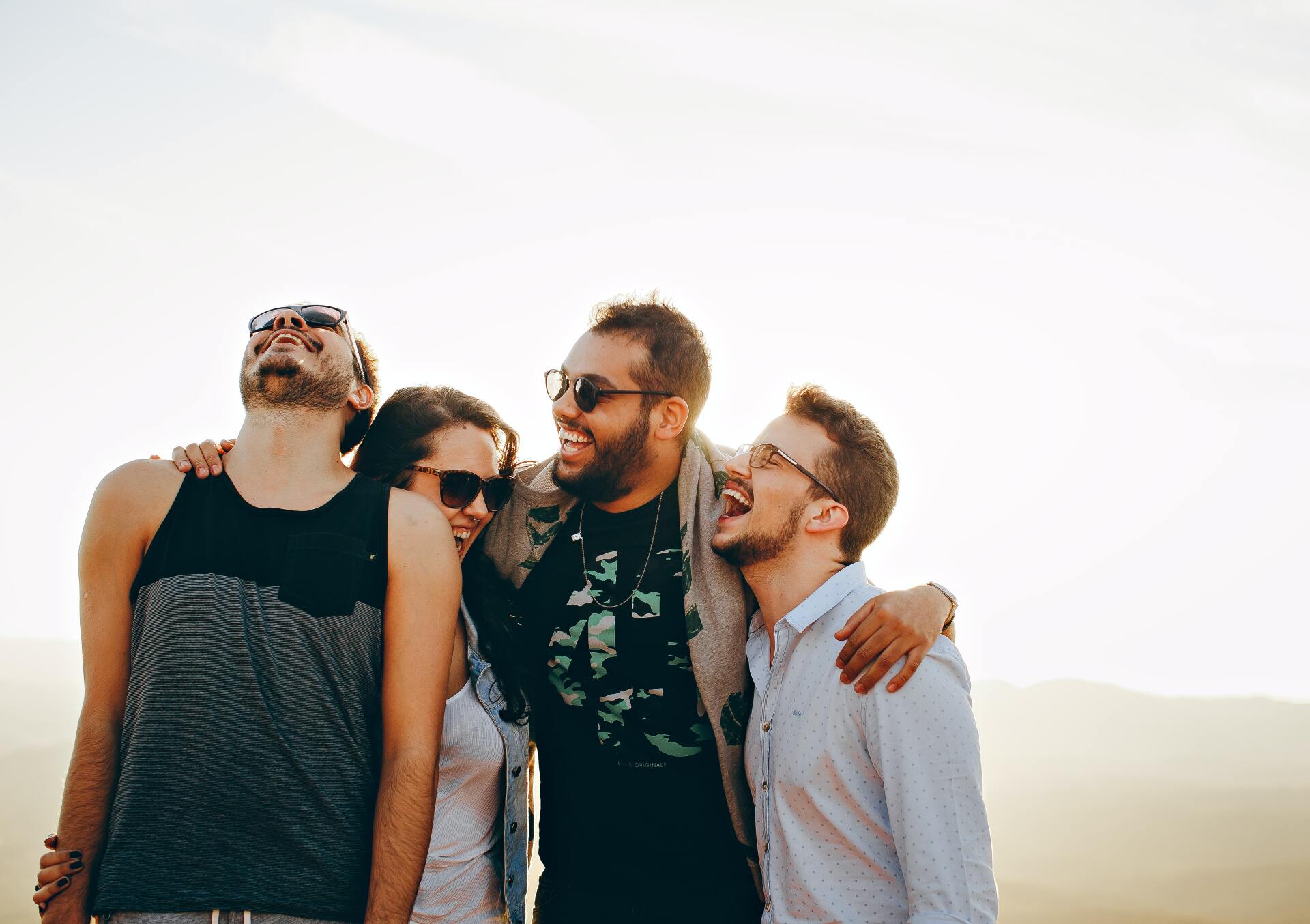 Group of four friends laughing together outdoors.