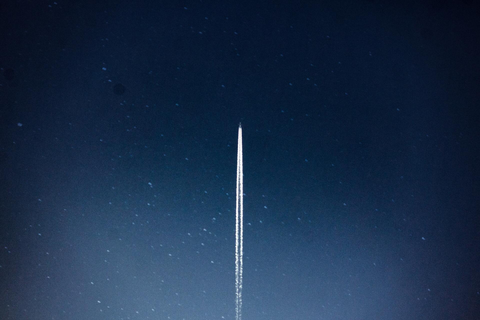 An airplane's contrail streaks across a dark blue sky with visible stars.