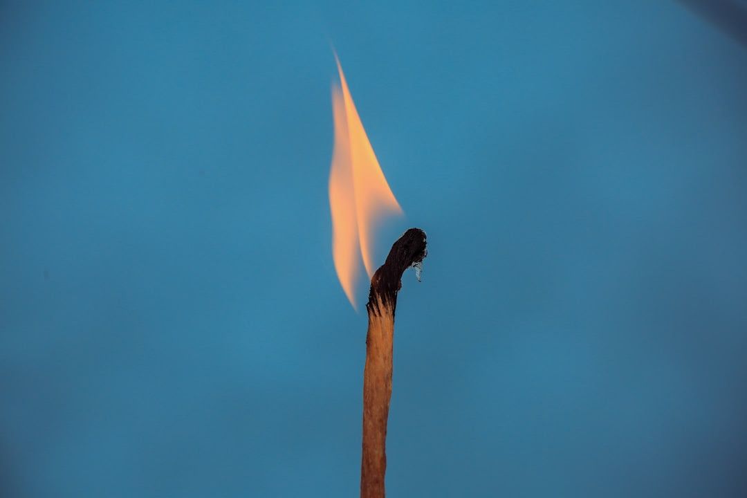 Burning matchstick with flame, against a blue background.