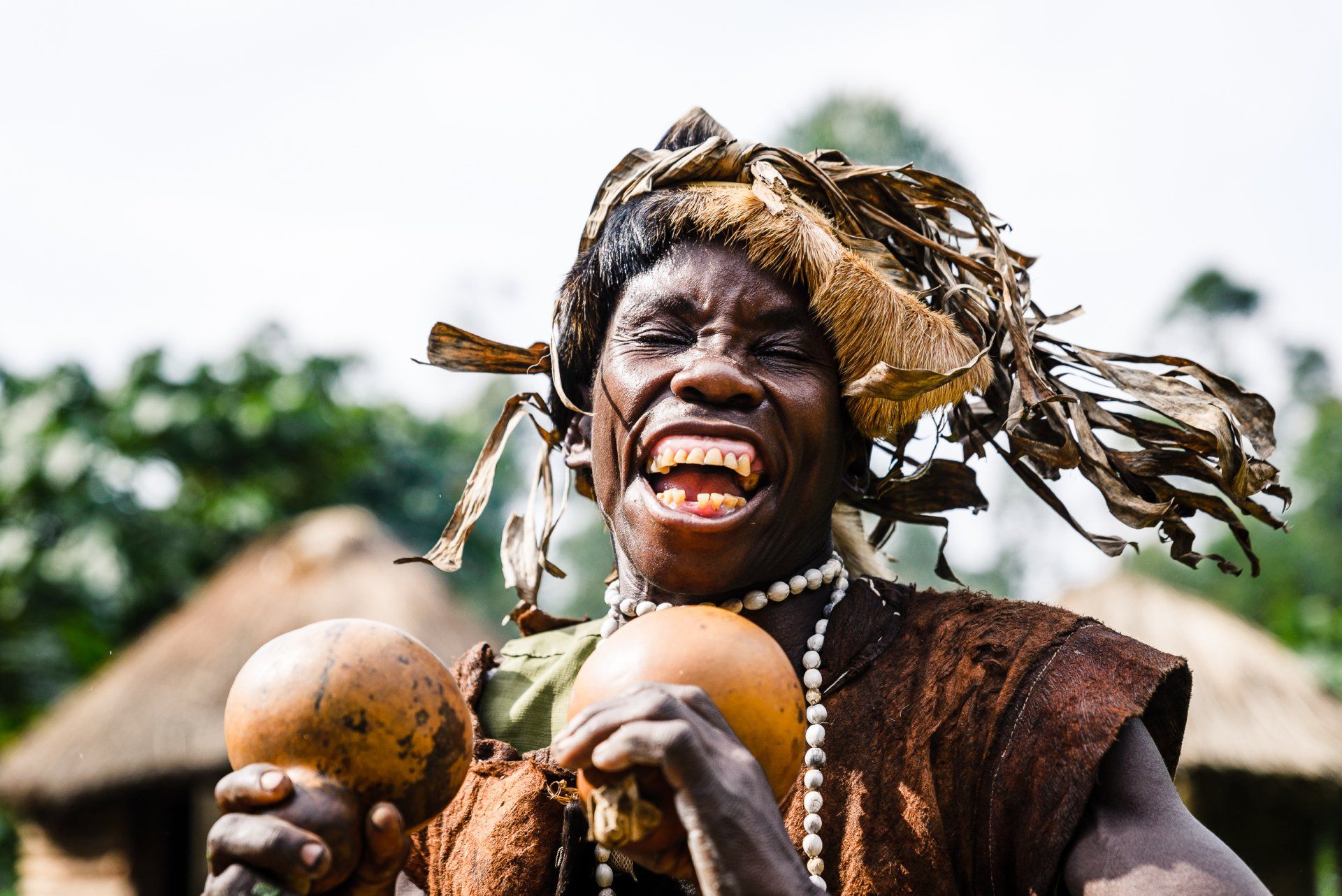 A person with an ecstatic expression holds two gourds, wearing traditional rustic clothing and a crown of dried leaves.