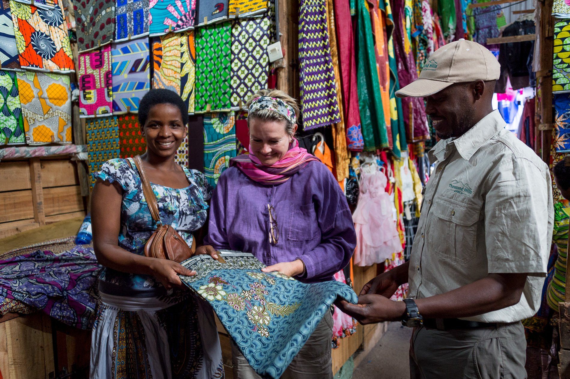 Three people standing in a shop filled with colorful patterned fabrics, examining a piece of blue patterned cloth.