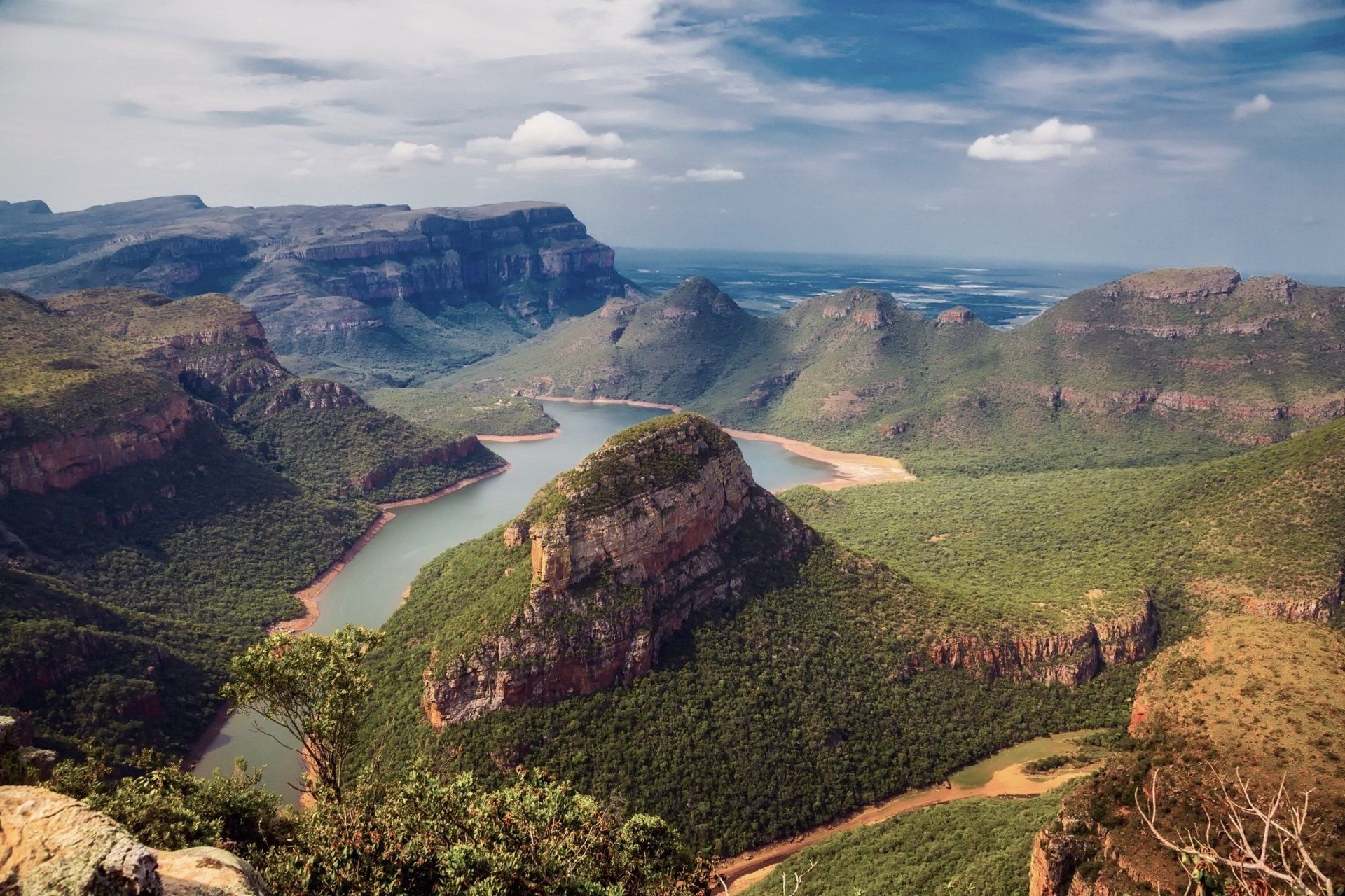 A winding river flows through the lush green valley and rugged cliffs of Blyde River Canyon under a cloudy sky.