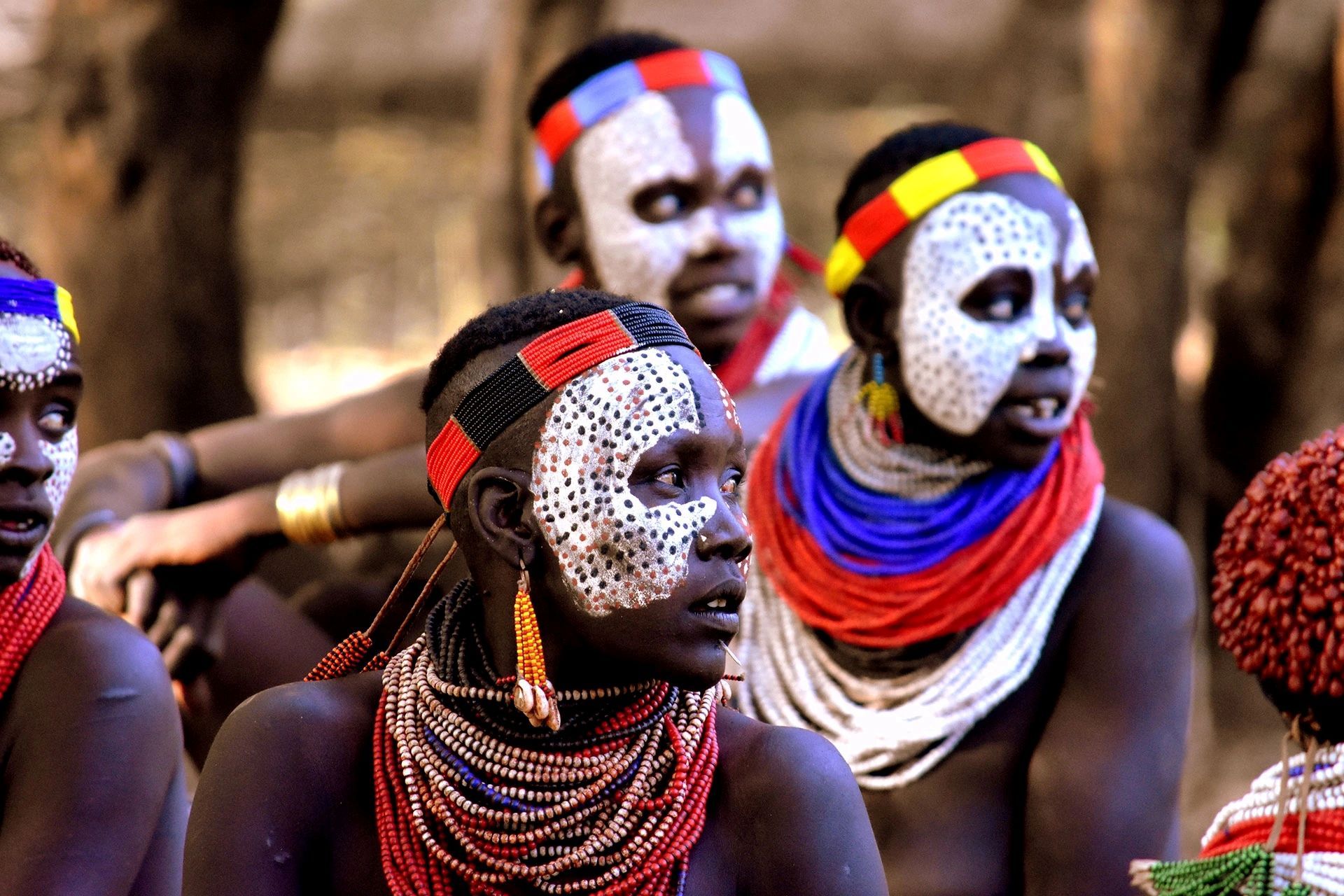 People from the Omo Valley adorned with white face paint, colorful beaded necklaces, and patterned headbands.