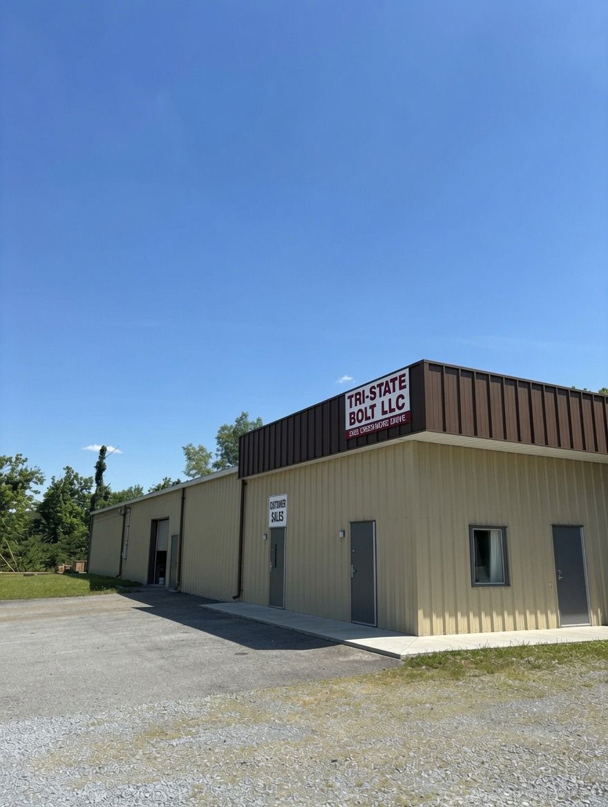 Small beige commercial building with a sign, gray doors, and gravel lot under a clear blue sky