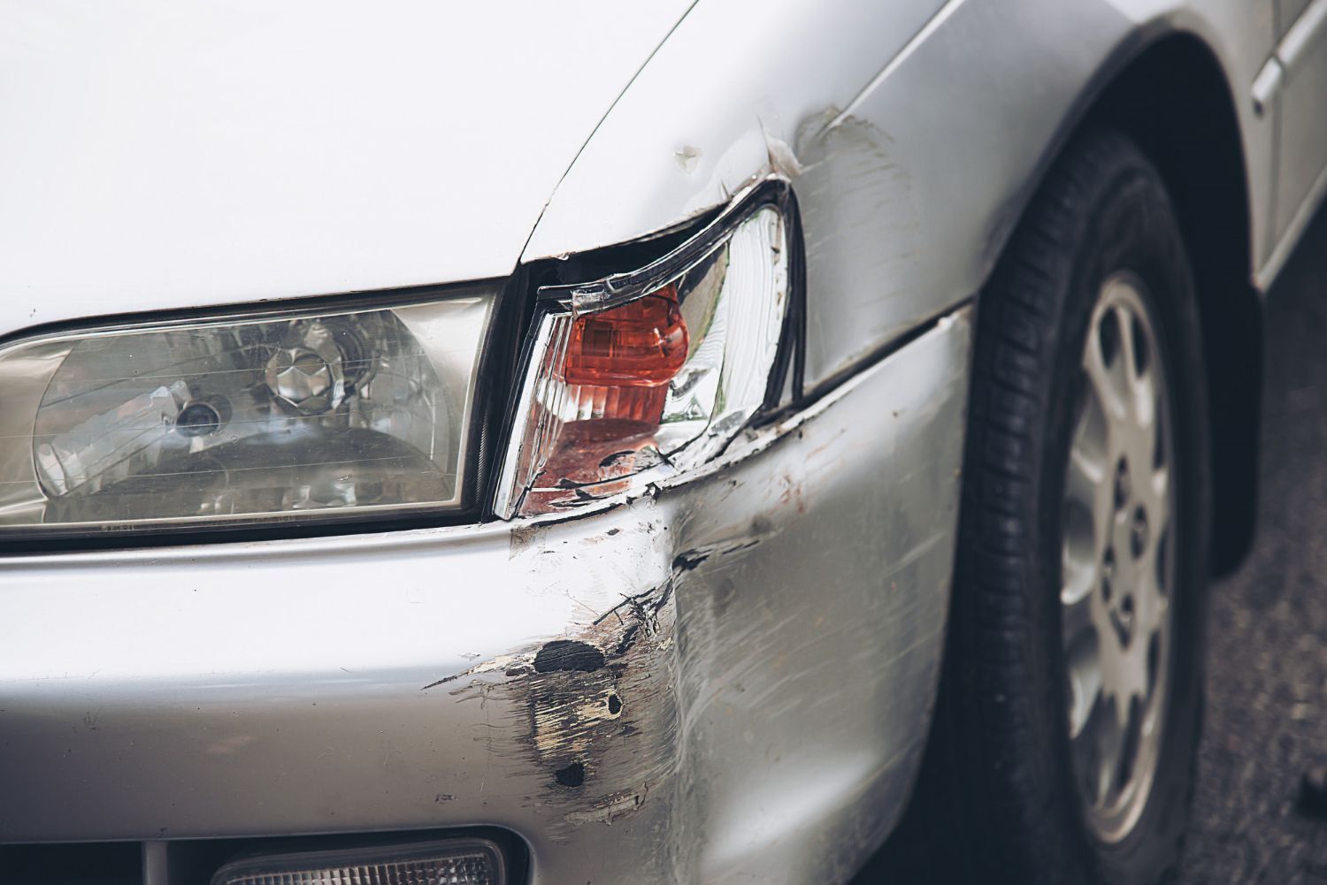 Silver car's front with damage to bumper and headlight.