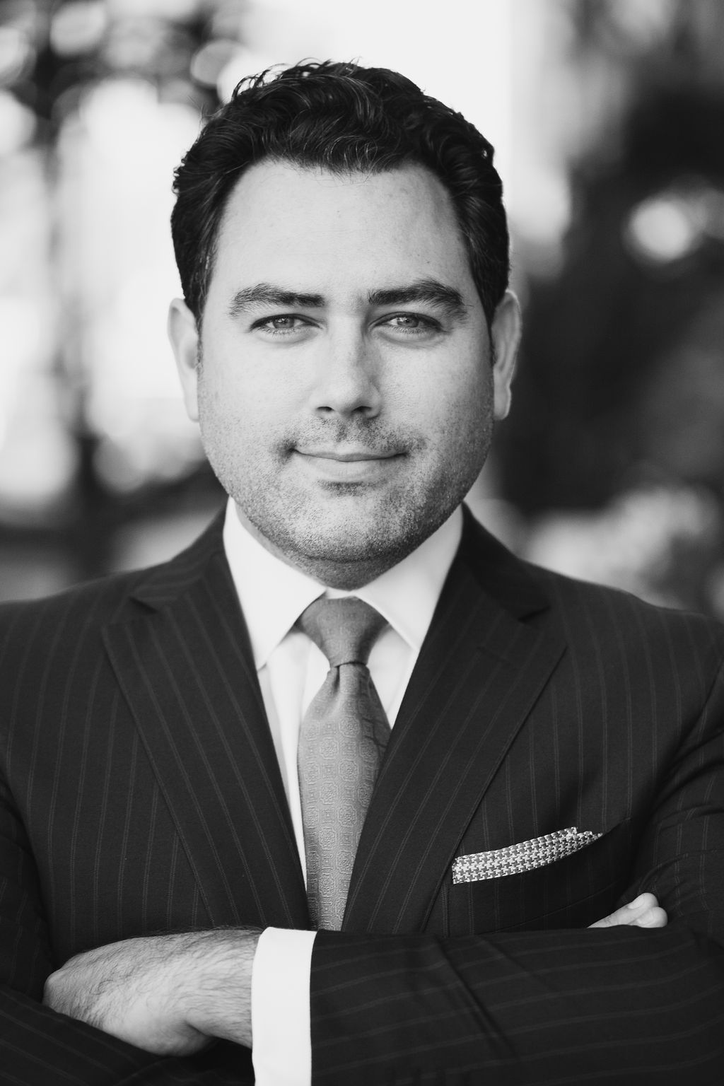 Man in suit, arms crossed, smiling slightly. Black and white portrait.