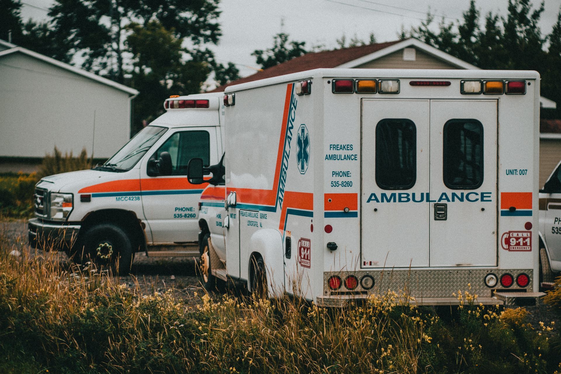 Two white ambulances with red and orange stripes parked outdoors near a building.