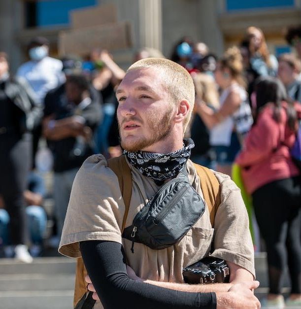 Blond man with a bandana and fanny pack looking off-camera at a demonstration.