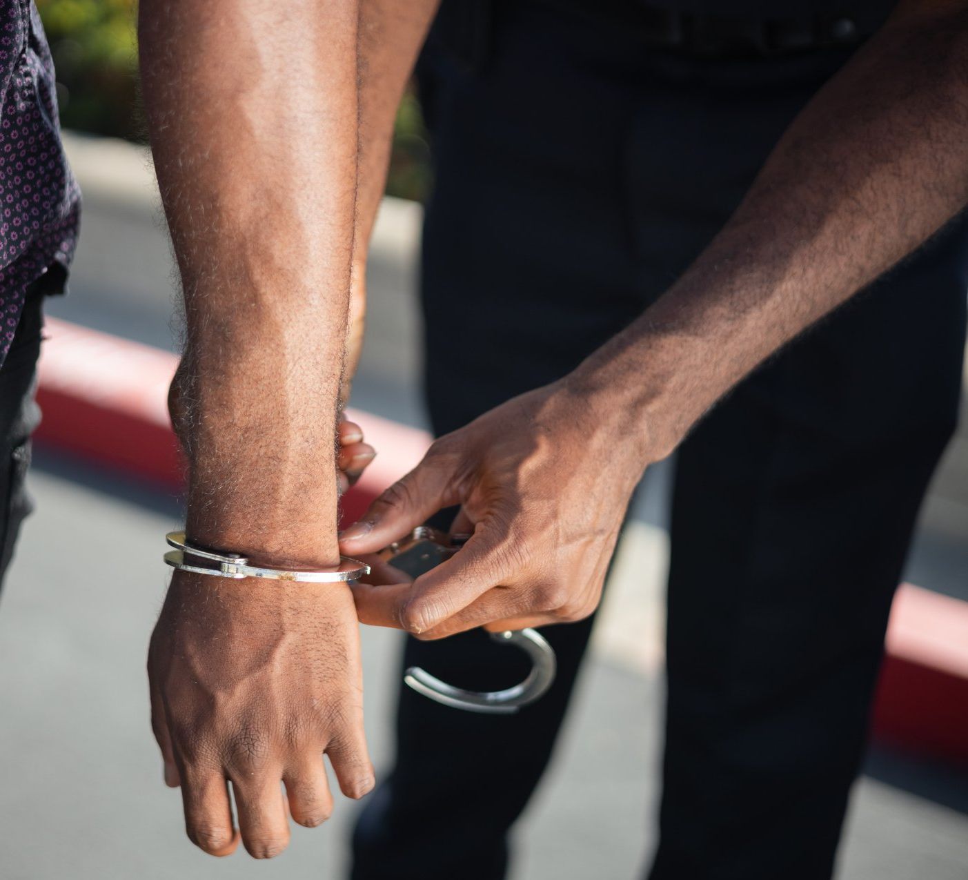 Hands of a person being cuffed by another's hands. One set of hands is in handcuffs.