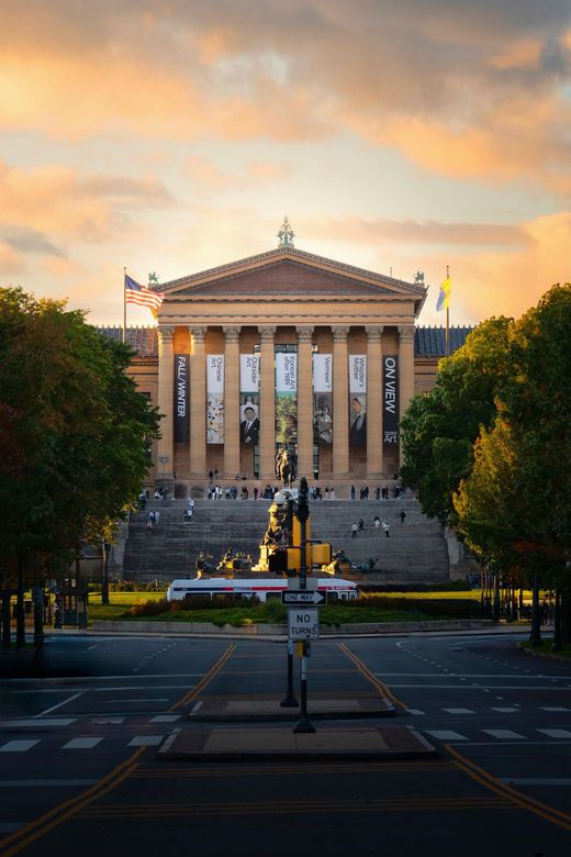 Philadelphia Museum of Art at sunset, facing a wide street with steps leading up to the entrance.
