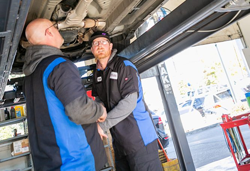 Two mechanics inspecting a vehicle underside in a garage lift area | Pro-Tech Autoworks
