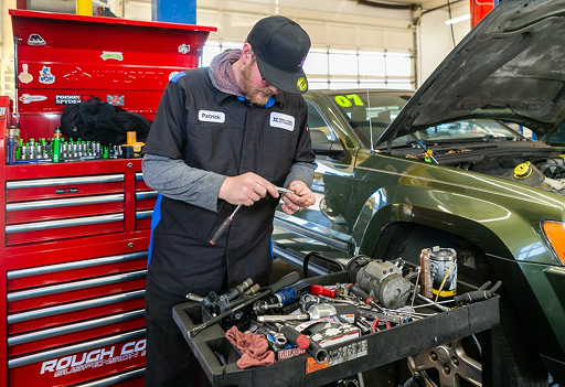 Mechanic working under an open hood beside a red tool chest in a garage | Pro-Tech Autoworks