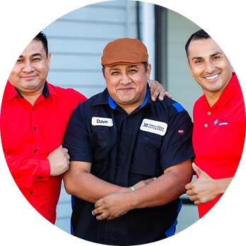 Three men in red and navy shirts pose together outdoors, smiling with arms crossed. | Pro-Tech Autoworks