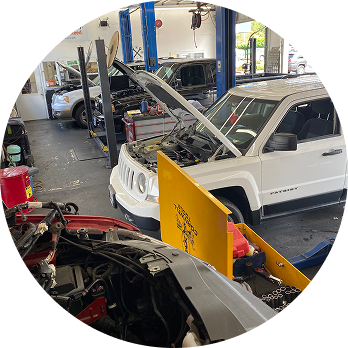 Auto repair shop with multiple cars, one hood open, and a yellow barrier in the foreground. | Pro-Tech Autoworks