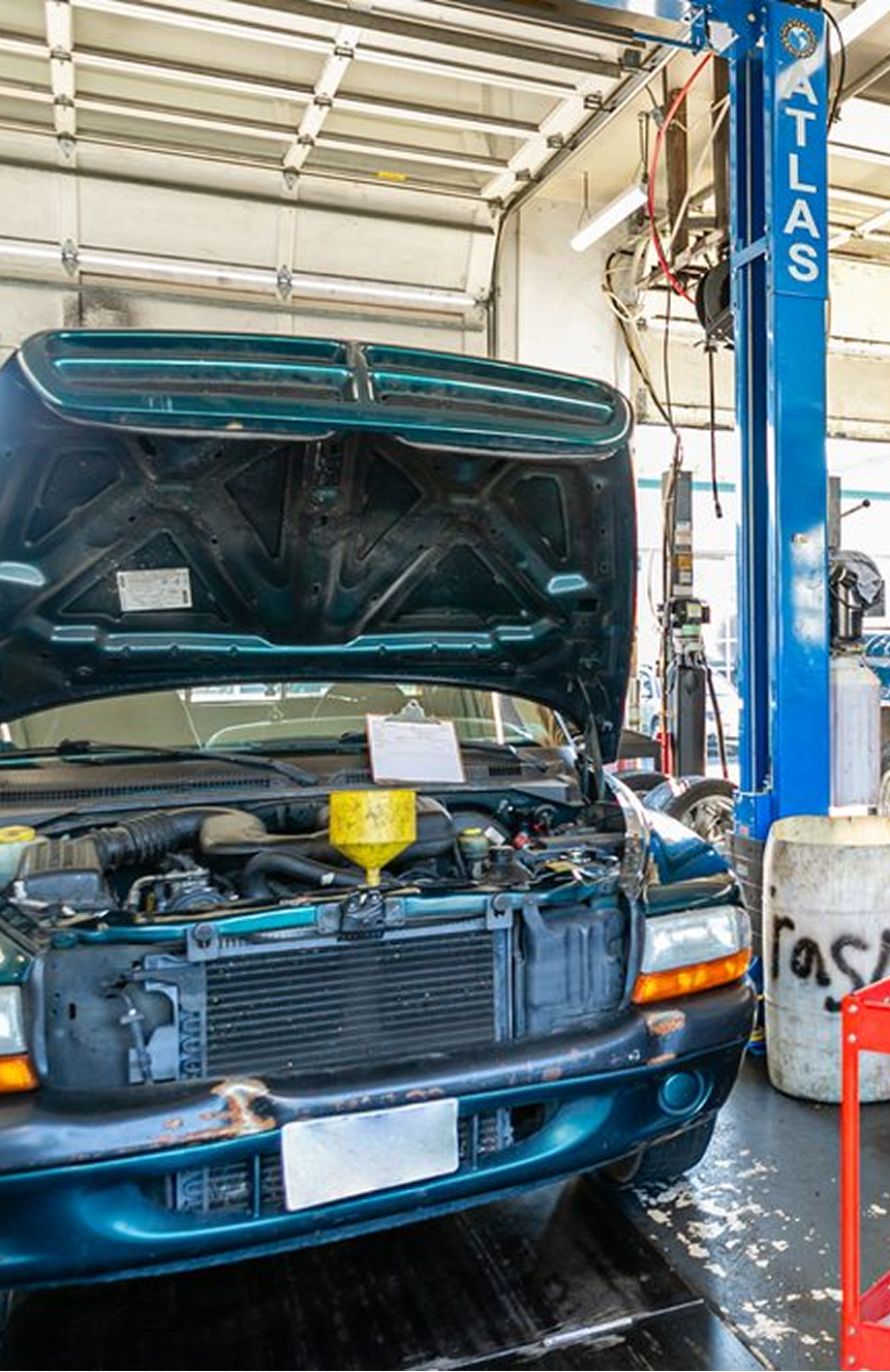 Blue van with hood open in an auto repair shop on a lift, with tools and equipment visible | Pro-Tech Autoworks