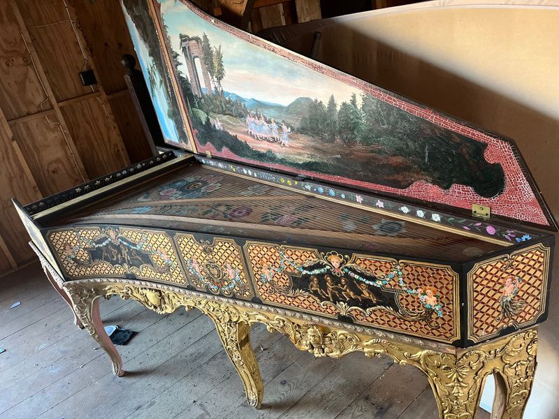 A piano with a painting on it is sitting on a wooden floor.