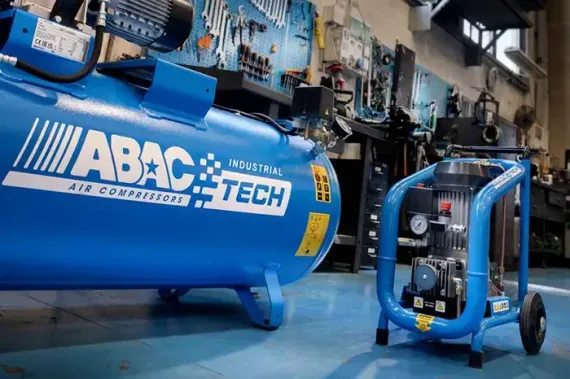 Compressore d'aria industriale Blue ABAC Tech installato in uno stabilimento, collegato a un'unità di pompaggio su ruote.