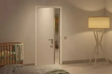 Una camera da letto con una porta bianca aperta, culla a sinistra e una lampada da terra alta a destra.