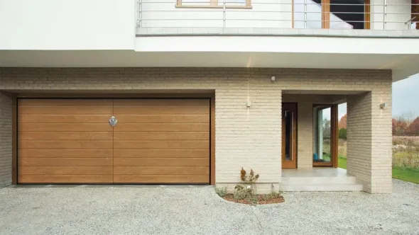 Esterno di una casa moderna con porta del garage in legno, ingresso principale e vialetto di accesso in ghiaia.