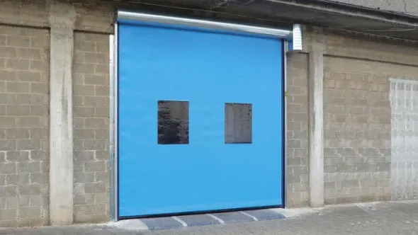 Porta avvolgibile industriale blu con due piccole finestre sulla facciata esterna di un edificio in cemento.
