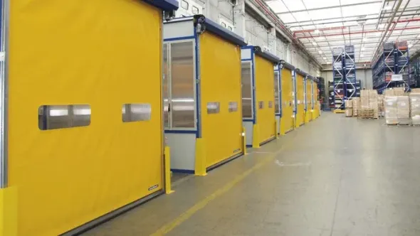 Porte industriali gialle fiancheggiano un corridoio luminoso di un magazzino, con scatole impilate in lontananza.