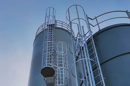 Silos industriali blu con scale metalliche sullo sfondo di un cielo limpido.