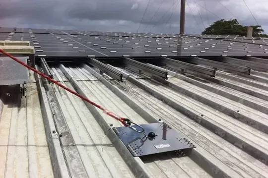 Installazione di pannelli solari sul tetto con binari di montaggio, fune di sicurezza rossa e attrezzi da lavoro su un tetto in lamiera ondulata.