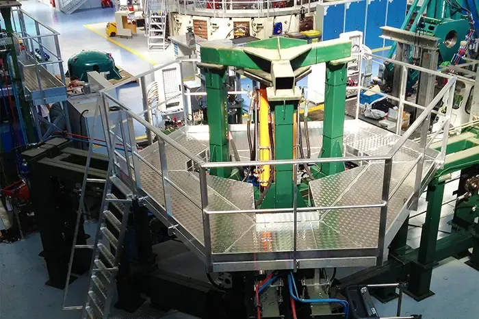 Macchinario industriale con componenti verdi e gialli su una piattaforma circolare in un ambiente di fabbrica.