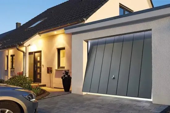 Esterno di una casa moderna al crepuscolo, con veranda illuminata e un grande portone del garage grigio.