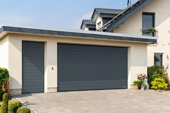 Esterno di una casa moderna con un grande portone del garage grigio e vialetto pavimentato.