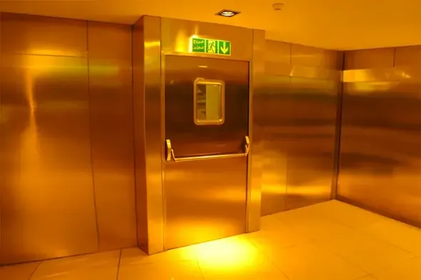 Interno vuoto di un ascensore in acciaio inossidabile con illuminazione calda gialla e una porta centrata nella cornice.