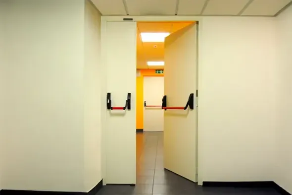 Apri le doppie porte che conducono a un corridoio luminoso con luce arancione e pareti bianche.