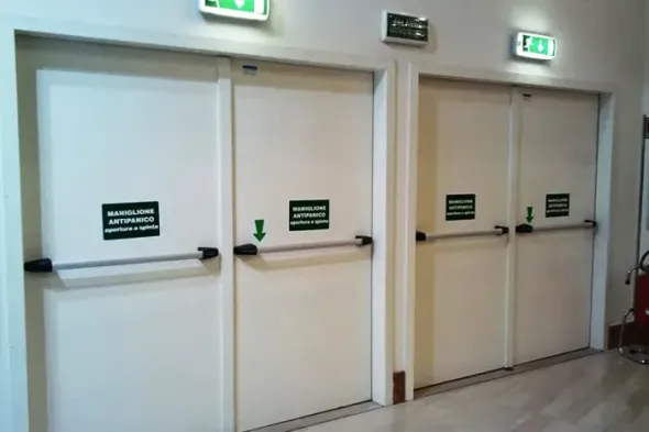 Tre porte di uscita di emergenza bianche con cartelli verdi USCITA in un corridoio