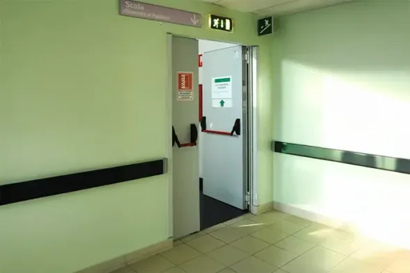 Corridoio ospedaliero vuoto con una parete verde e una porta aperta che conduce a un altro corridoio.