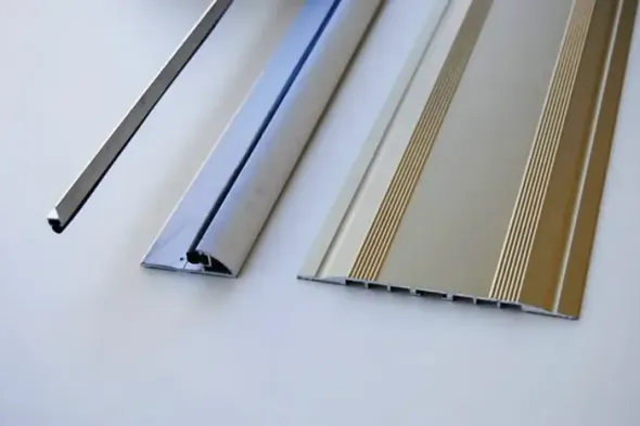 Tre listelli decorativi in bianco, argento e oro, disposti diagonalmente su una superficie bianca