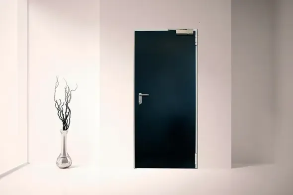 Stanza minimalista bianca con porta blu scuro e un piccolo vaso di rami spogli sulla sinistra.