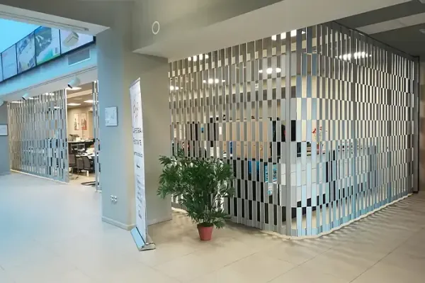 Corridoio moderno di un centro commerciale con vetrina, recinzione a doghe metalliche e una pianta in vaso nelle vicinanze.