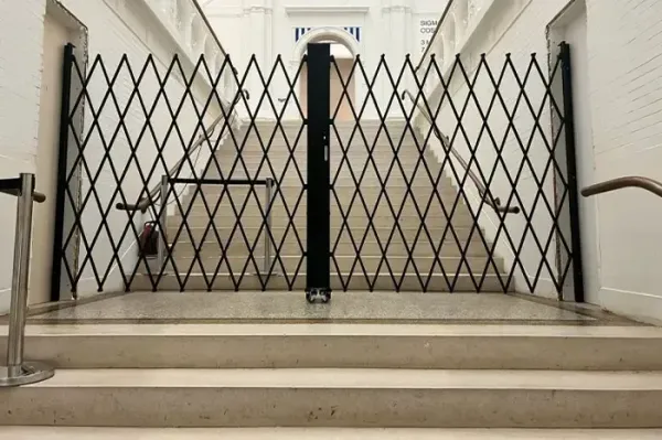 Cancello a soffietto chiuso che blocca le scale in un corridoio beige