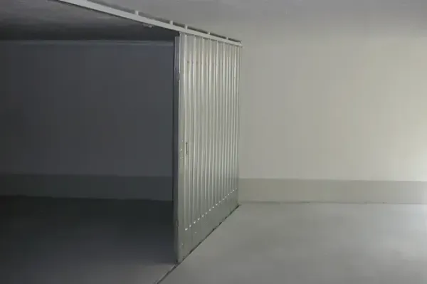 Stanza industriale grigia e vuota con un grande container o divisorio metallico sulla sinistra.