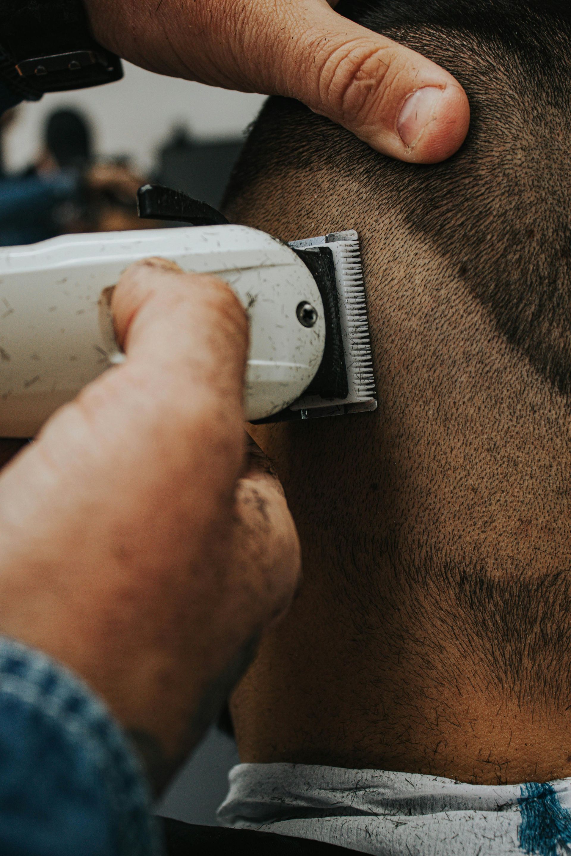 Close-up of a barber trimming the back of a person’s neck with electric clippers.