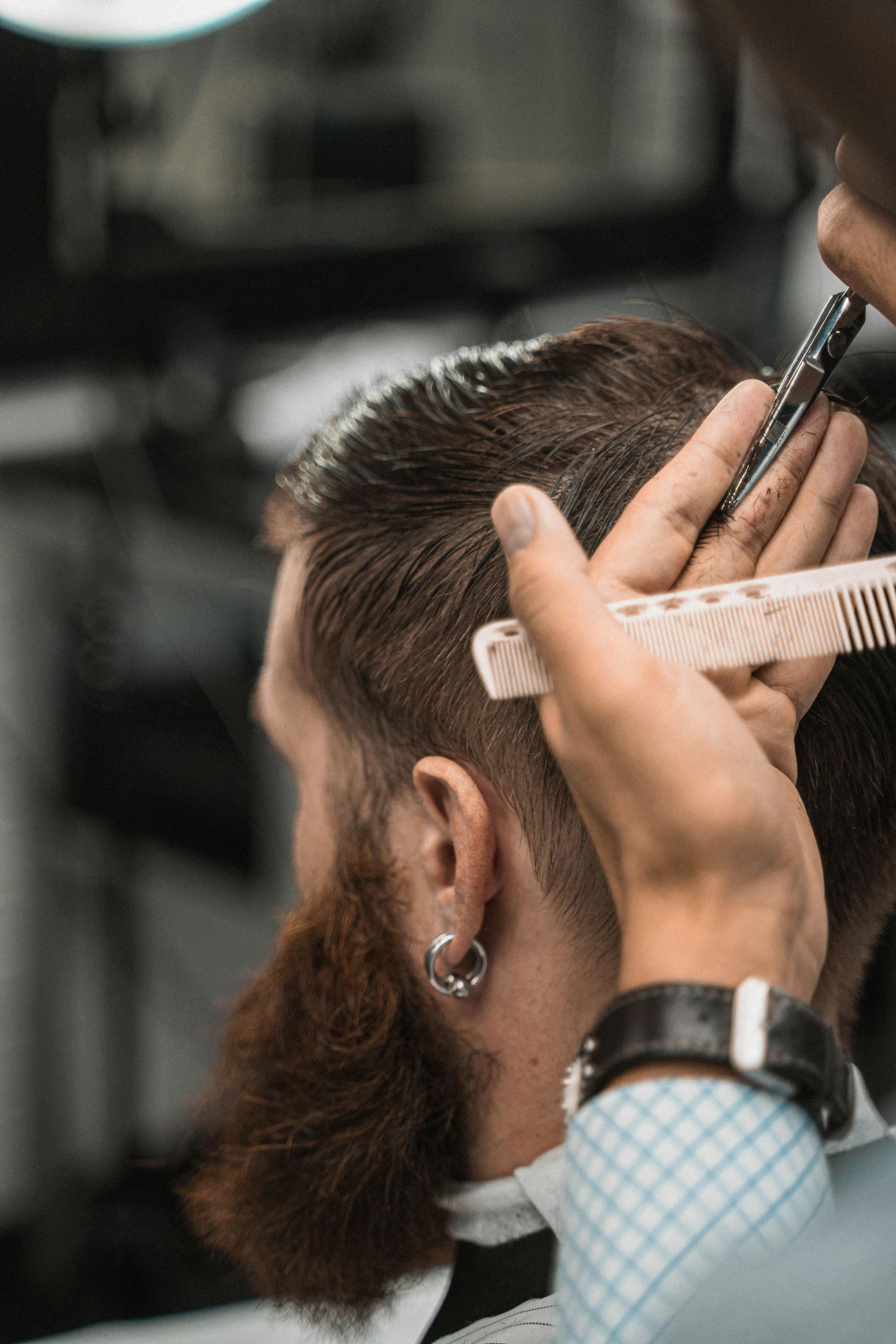 Barber trimming a bearded client’s hair with clippers and a comb in a salon