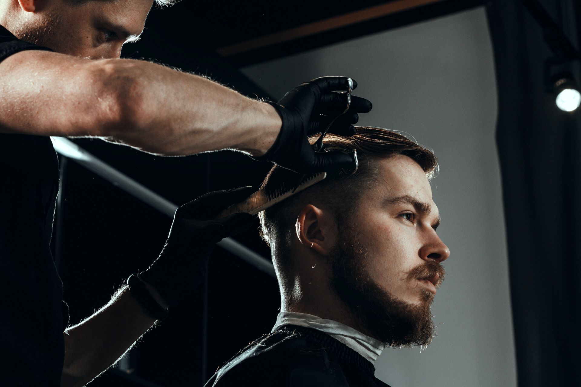 Barber trimming a man's hair with clippers in a dimly lit barbershop