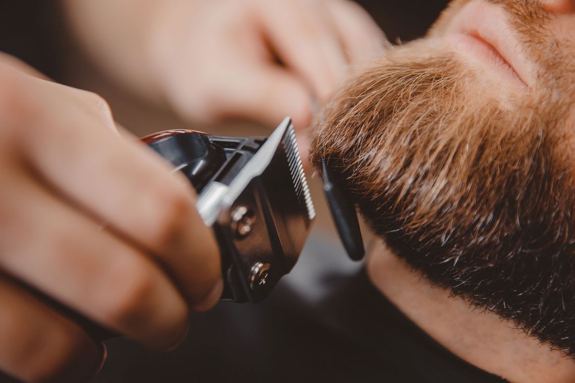 Barber trimming a man’s beard with electric clippers in a close-up salon scene