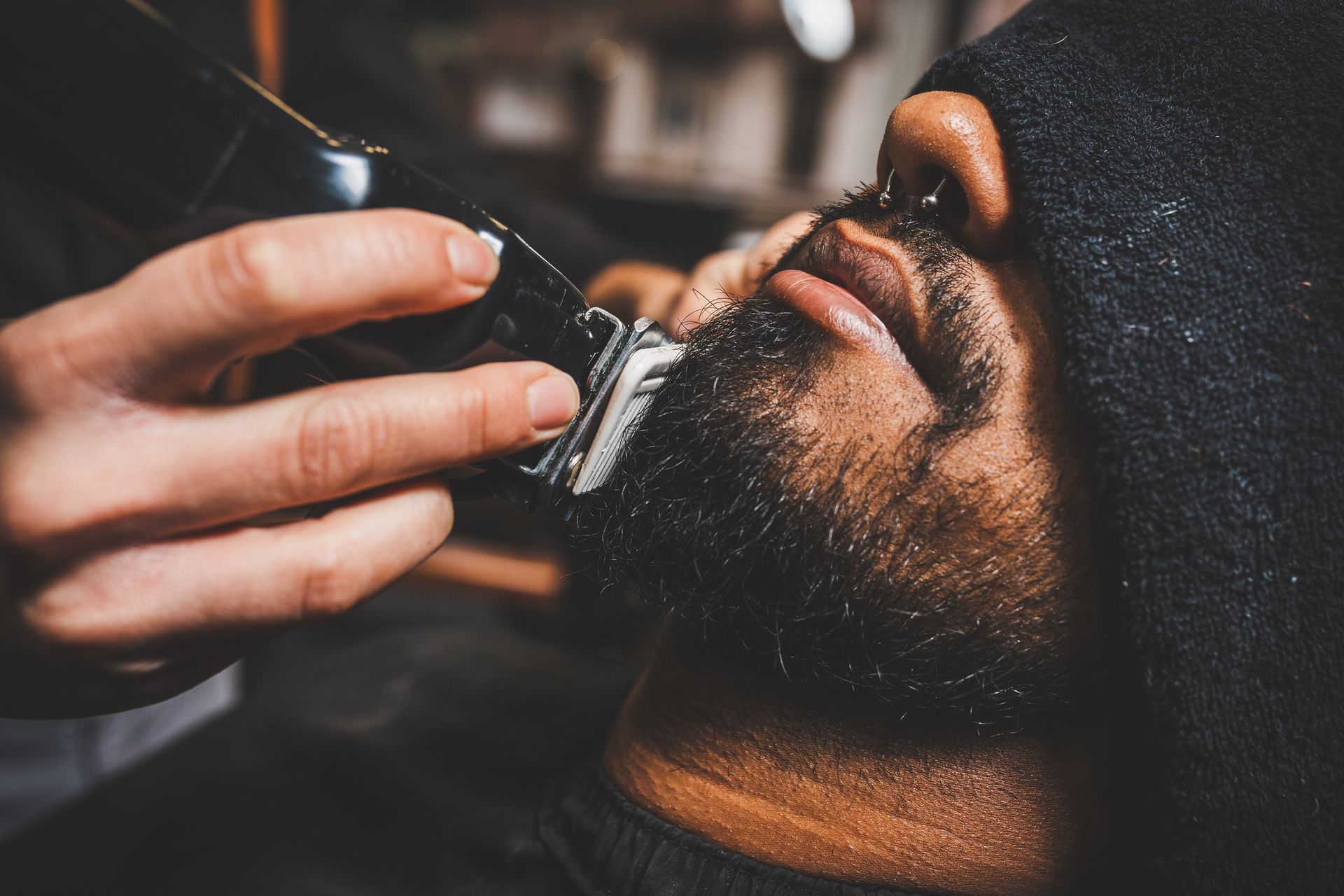 Bearded man getting his beard trimmed with electric clippers in a close-up salon scene