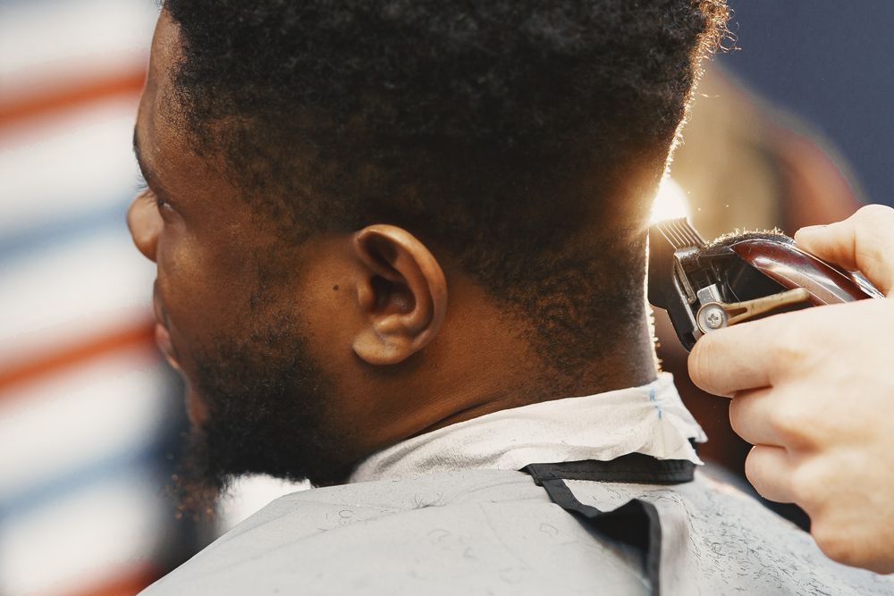 Barber trimming a man's hair with clippers, close-up side view