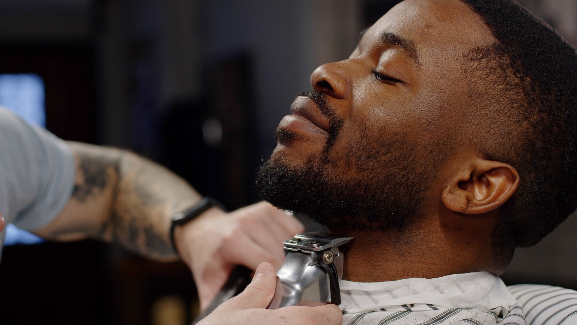 Barber trimming a customer’s beard with electric clippers in a salon chair