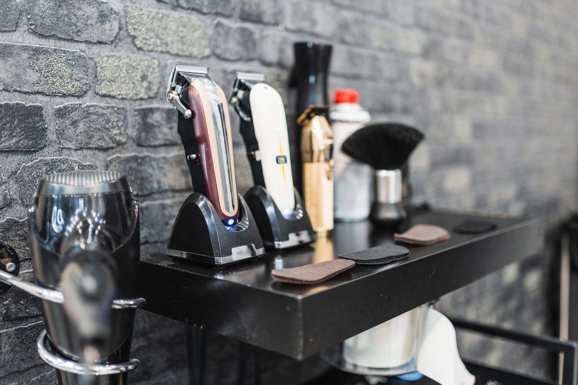 Barber tools and clippers organized on a black shelf against a gray brick wall