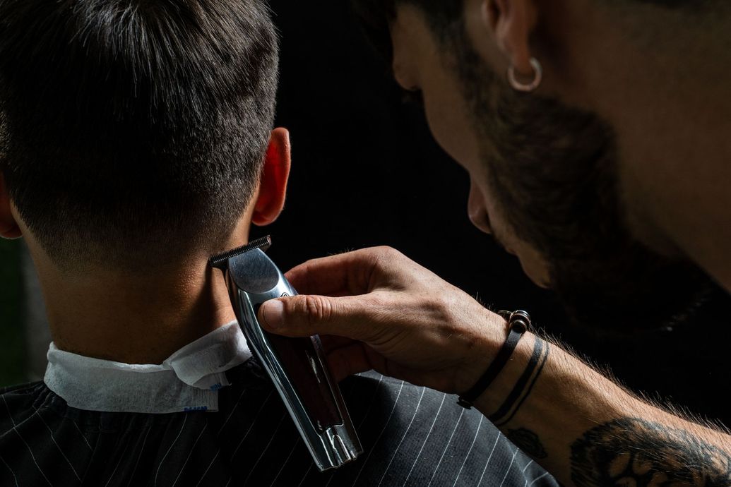 Barber trimming the back of a customer’s neck with electric clippers in a dark salon